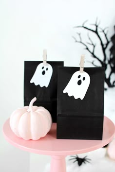 two bags with ghost faces on them are sitting on a pink cake plate next to a white pumpkin