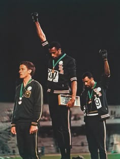 three men standing on top of a soccer field holding their hands up in the air