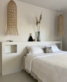 a bed with white sheets and pillows in a bedroom next to two hanging baskets on the wall