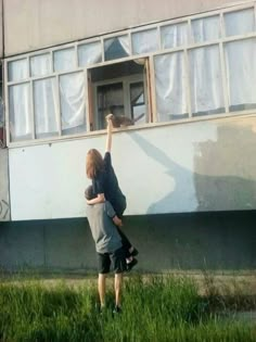 two people reaching up into the air to grab something out of an open window on top of a building