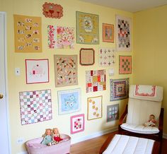 a baby's room decorated in pastel colors with quilts on the wall