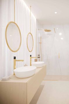 a bathroom with two sinks and a shower in the background, all white walls are decorated with gold accents