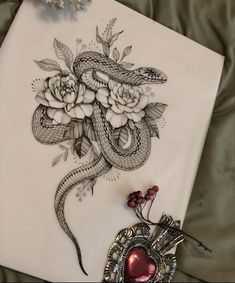 a drawing of a snake and flowers on a sheet of paper next to a brooch