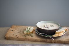 a bowl of soup on a wooden cutting board with bread and garnishes