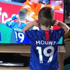 a young boy standing in front of a tv holding his hands up to his head