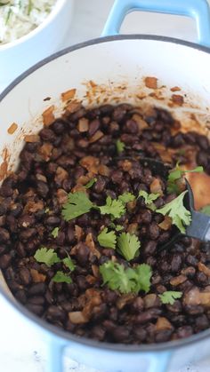 a pot filled with beans and cilantro on top of a table next to another bowl