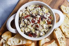 a white bowl filled with food sitting on top of a cutting board next to bread