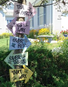 a tree with several signs attached to it in front of a house that says tea party this way