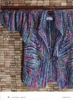 a colorful knitted jacket hanging on a brick wall in front of a wooden frame