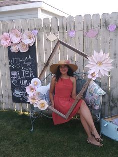 a woman sitting on a lawn chair with flowers in front of her and a chalkboard sign behind her