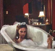 a woman sitting in a bathtub holding a cell phone to her ear and wearing a tiara