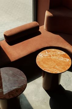 an orange couch and two tables in front of a glass door with the sun shining on it