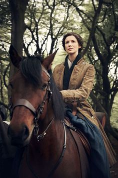 a woman riding on the back of a brown horse through a forest filled with trees