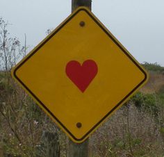 a yellow street sign with a red heart on it