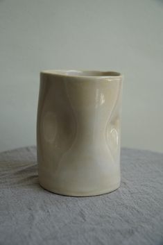 a white cup sitting on top of a table next to a gray cloth covered wall