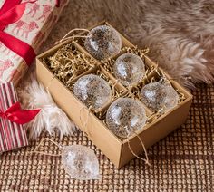 a box filled with christmas ornaments next to a wrapped gift bag and two empty glass ornament balls