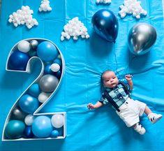 a baby laying on top of a blue table cloth next to balloons and number 2