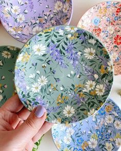 a person holding a plate with flowers on it in front of other plates that have different designs