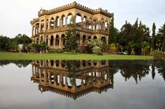 an old building sitting on top of a lush green field next to a body of water