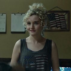 a woman with curly hair standing in front of an american flag wall hanging on the wall