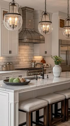 a kitchen island with stools and lights hanging over it