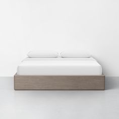 a bed with two pillows on top of it in front of a white wall and floor