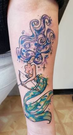 a woman's leg with a watercolor tattoo design on her left arm and the image of a mermaid holding a star