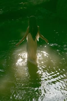 a woman in a body of water with her arms spread out to the side as she stands