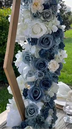 a tall blue and white flower arrangement on top of a wooden table in the grass