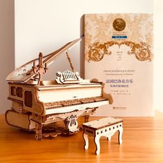 a wooden model of a grand piano and stool on a table next to a book