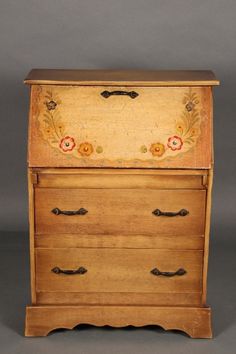 an old wooden dresser with flowers painted on the top and bottom drawer, sitting against a gray background