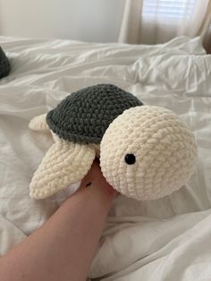 a hand holding a stuffed turtle on top of a bed