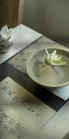 a white plate sitting on top of a table next to a bowl filled with flowers