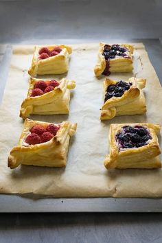 several pastries with raspberries and blueberries in them on top of parchment paper