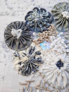 several different types of fabric flowers on a piece of white cloth with beads and sequins