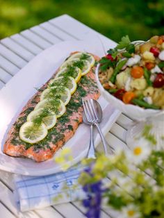 a white plate topped with salmon next to a bowl of salad and a fork on top of a table