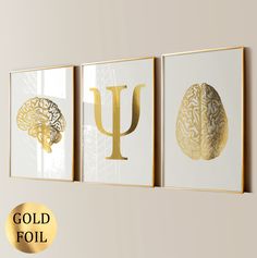 three gold foil prints with the letter u and brain images on them, against a beige wall