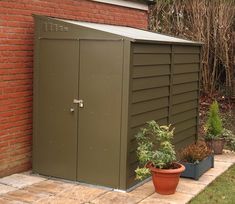 there is a small green shed next to a brick wall and potted plants on the ground