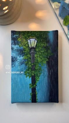 a painting of a lamp post in the rain on a white table next to a vase with flowers