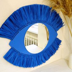 a blue eye shaped mirror sitting on top of a white table next to a vase