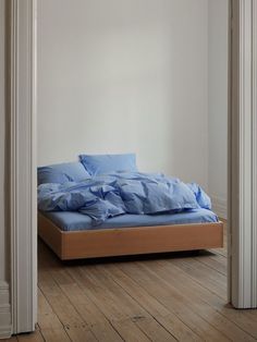 an unmade bed with blue sheets in a white walled room next to a wooden floor