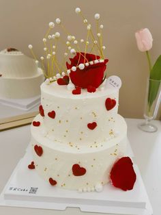 a three tiered wedding cake with red roses and hearts on it, sitting on a table