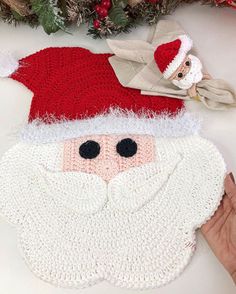 a crocheted santa clause ornament on a table with christmas decorations around it