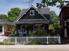 a white picket fence is in front of a house with red flowers and greenery