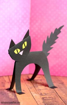 a paper cut out of a black cat with glowing eyes and tail, standing on a wooden floor