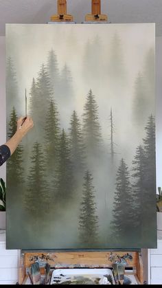 a person is painting a forest scene on canvas