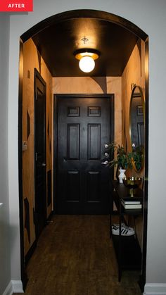 an entry way with a black door and mirror on the side wall, next to a table with a potted plant