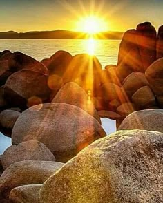 the sun is setting over some rocks by the water