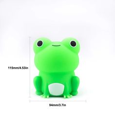 a green frog toy sitting on top of a white floor next to a ruler with its eyes wide open