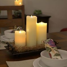 three lit candles sitting on top of a table next to plates and bowls with napkins